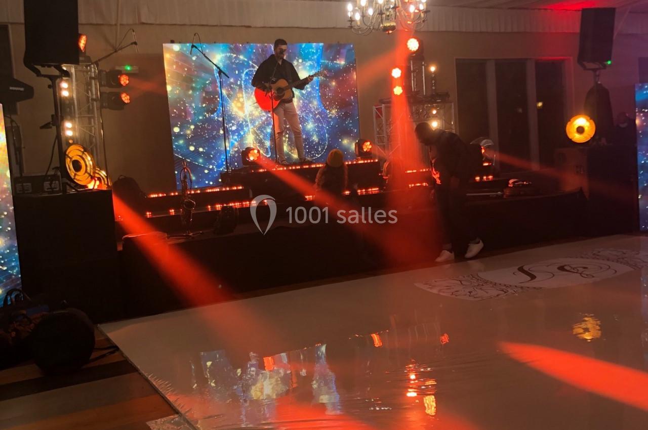 Un musicien joue de la guitare sur une scène éclairée par des projecteurs rouges, avec un écran étoilé en arrière-plan.