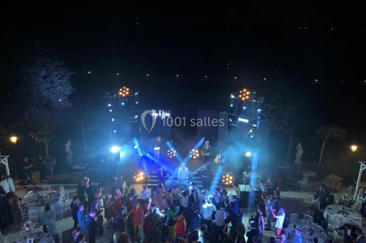 Vue nocturne d'une scène en plein air avec un groupe jouant devant une foule dans une ambiance festive éclairée.