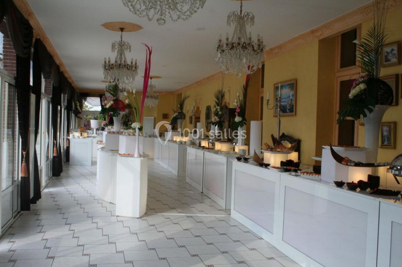Salle lumineuse avec de longues tables blanches alignées, décorées de fleurs et de plats pour un buffet.