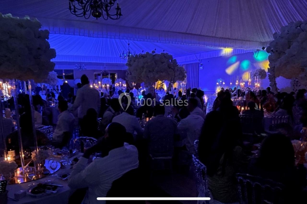 Salle de réception sombre avec des invités assis, éclairée par des lumières tamisées et des décorations florales blanches.