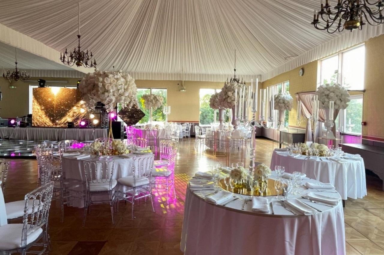 Salle de réception élégante avec tables décorées de fleurs blanches, chaises transparentes et éclairage tamisé.