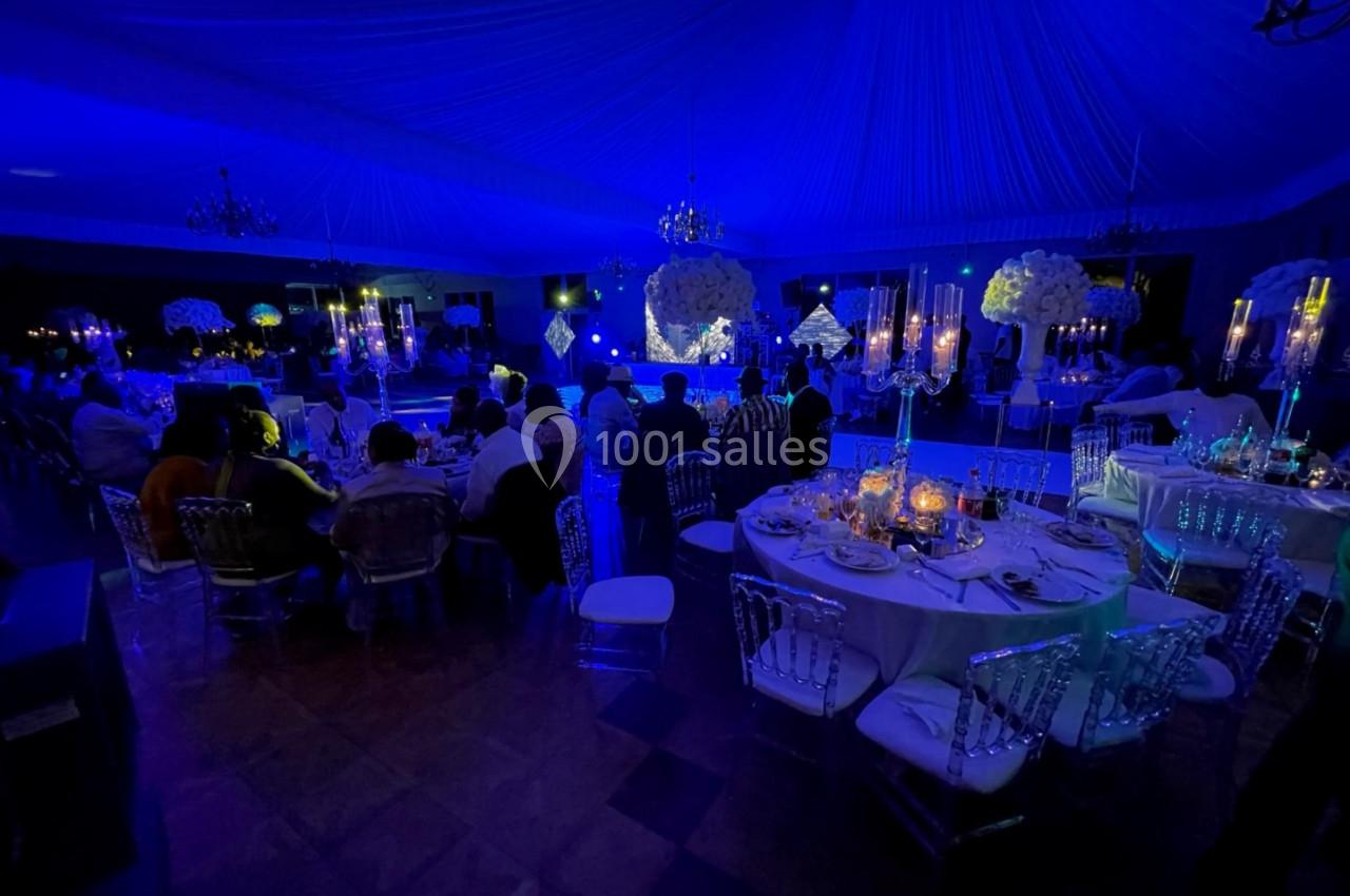 Salle de réception illuminée en bleu avec des tables décorées, des chandeliers et des invités assis.