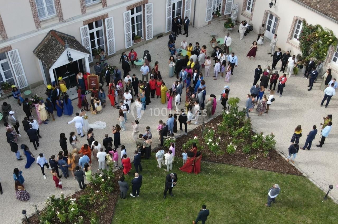 Vue aérienne d'un rassemblement de personnes dans la cour d'un bâtiment avec jardin et parterres de fleurs.