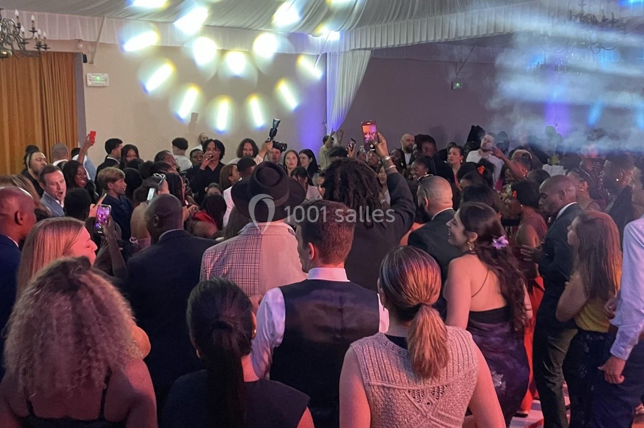 Groupe de personnes rassemblées dans une salle éclairée, certaines dansent tandis que d'autres observent ou prennent des…