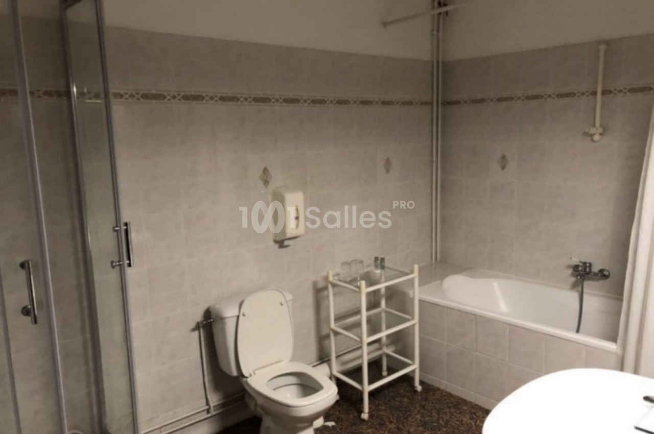 Salle de bain avec douche vitrée, baignoire, toilettes, porte-serviettes et murs carrelés dans des tons clairs.