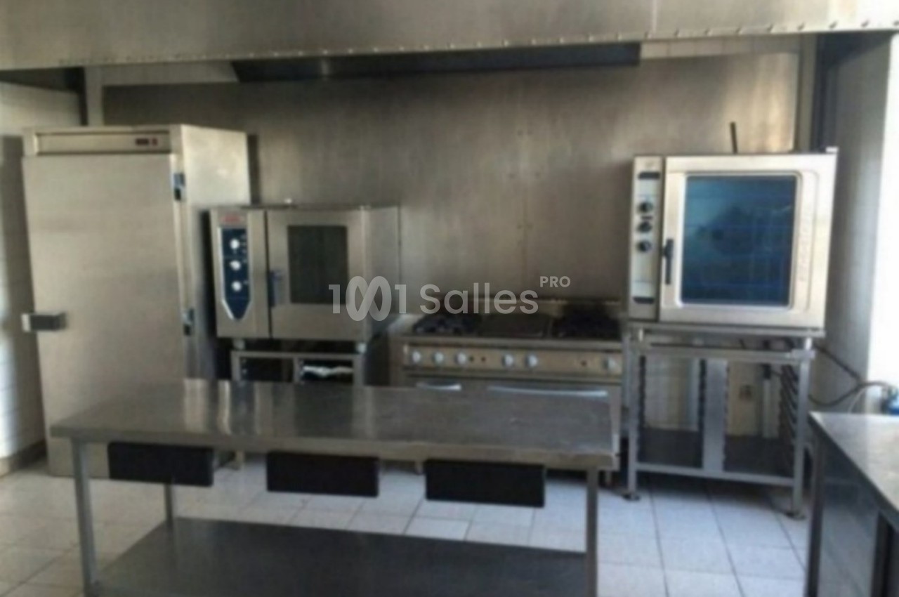 Cuisine professionnelle équipée avec four, réfrigérateur, plaques de cuisson et plan de travail en inox.