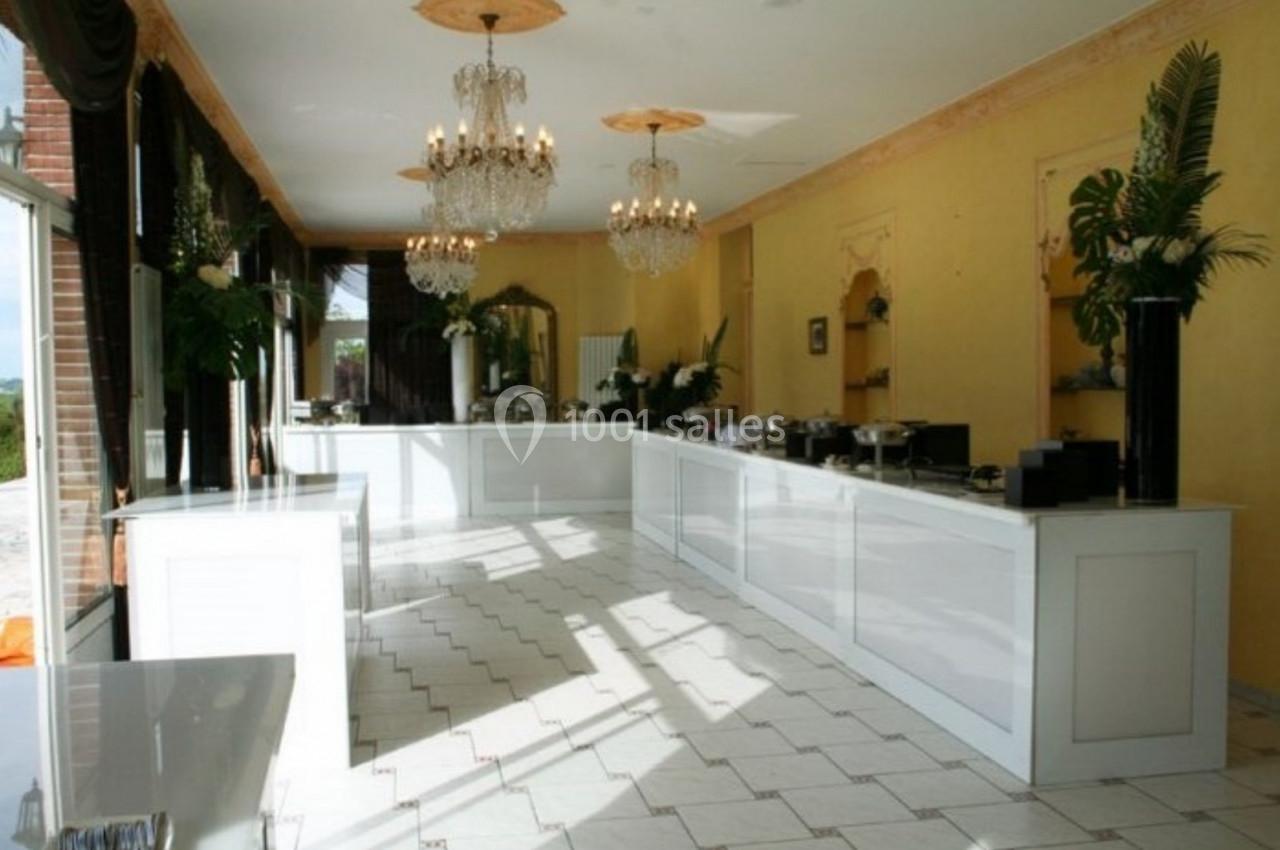 Salle lumineuse avec comptoirs blancs, lustres en cristal, carrelage clair et décorations végétales.