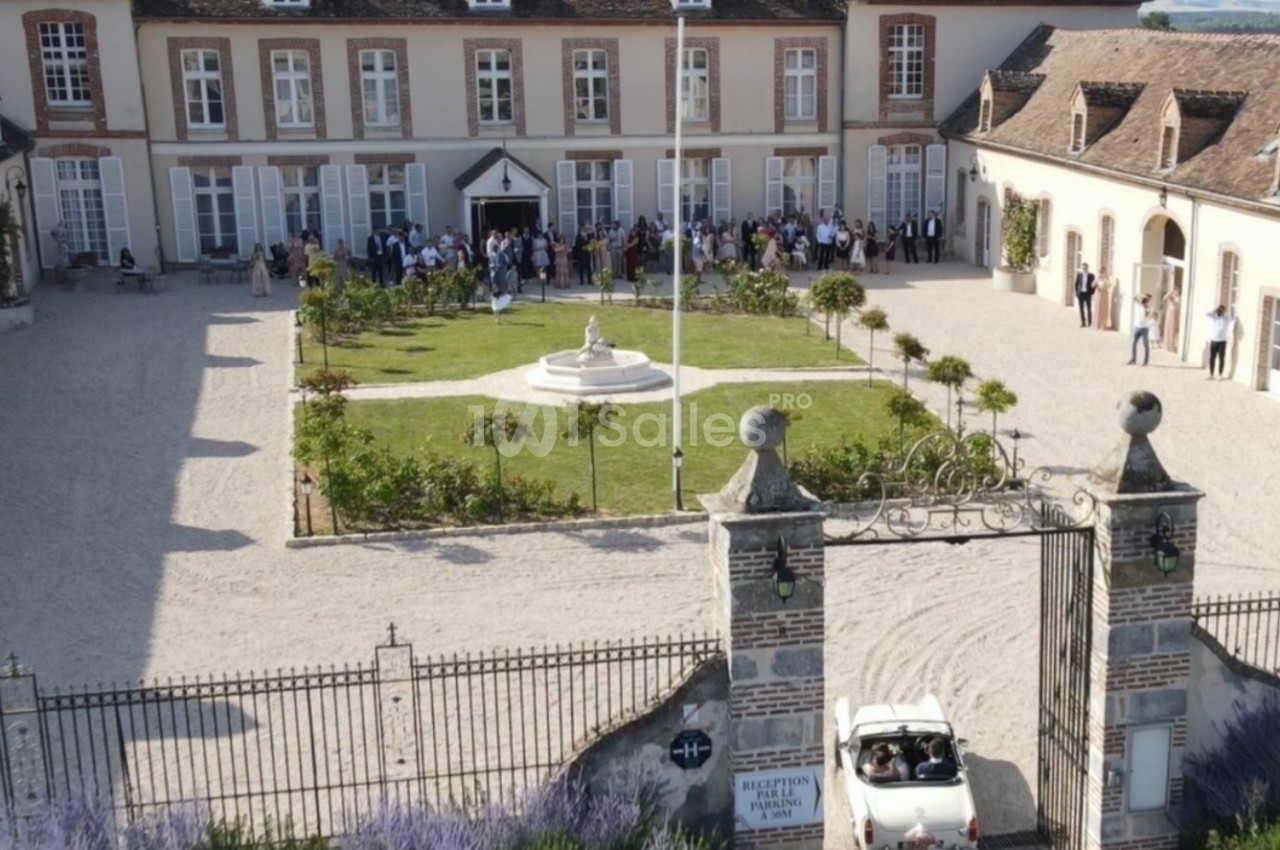 Vue aérienne d'une cour intérieure avec jardin central, entourée de bâtiments anciens, et une voiture blanche entrant par le…