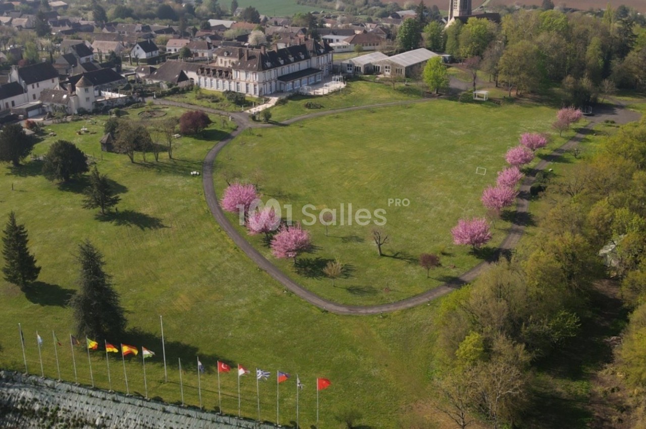 Vue aérienne d'un parc avec pelouse, arbres en fleurs roses, drapeaux alignés et bâtiments résidentiels en arrière-plan.