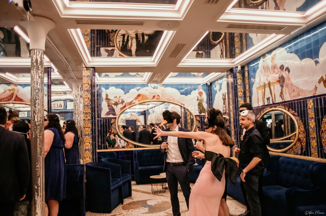 Location salle Paris 2 (Paris) - Aux Belles Poules #12 Personnes élégamment vêtues discutant et prenant des photos dans une salle ornée de miroirs et de fresques colorées.
