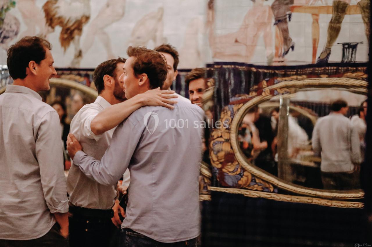 Location salle Paris 2 (Paris) - Aux Belles Poules #13 Un groupe d'hommes discutant et s'embrassant dans un intérieur décoré avec des miroirs et des motifs artistiques.