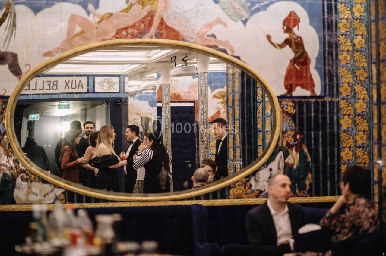 Location salle Paris 2 (Paris) - Aux Belles Poules #14 Un groupe de personnes discutant dans un intérieur décoré de fresques colorées, reflété dans un grand miroir ovale.