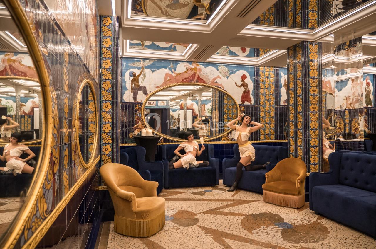 Location salle Paris 2 (Paris) - Aux Belles Poules #17 Deux femmes posent dans un salon richement décoré avec des miroirs, des fresques colorées et des fauteuils élégants.