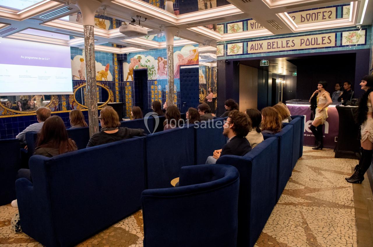 Location salle Paris 2 (Paris) - Aux Belles Poules #9 Personnes assises dans une salle colorée avec des fresques murales, regardant une présentation projetée sur un écran.