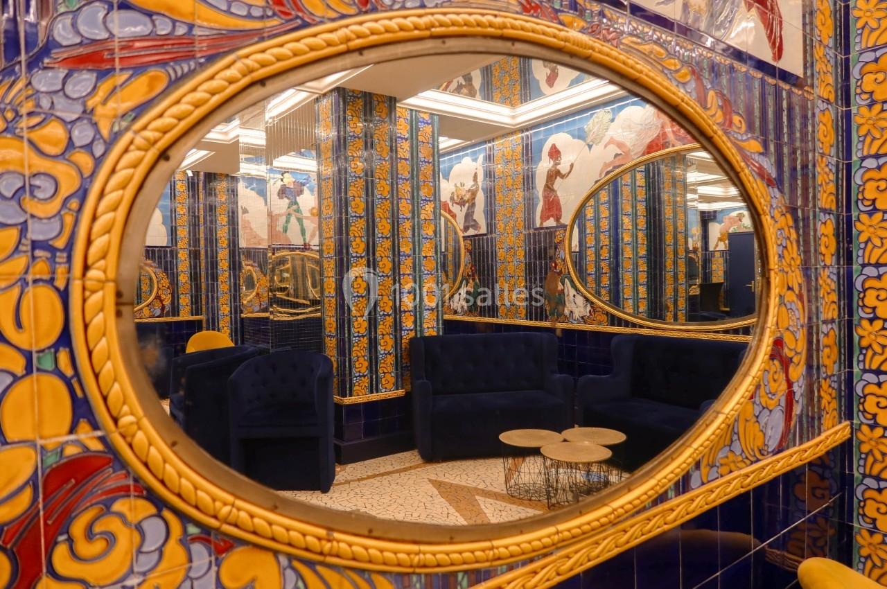 Location salle Paris 2 (Paris) - Aux Belles Poules #7 Miroir ovale reflétant un salon avec canapés bleus, tables basses et murs ornés de carreaux colorés.