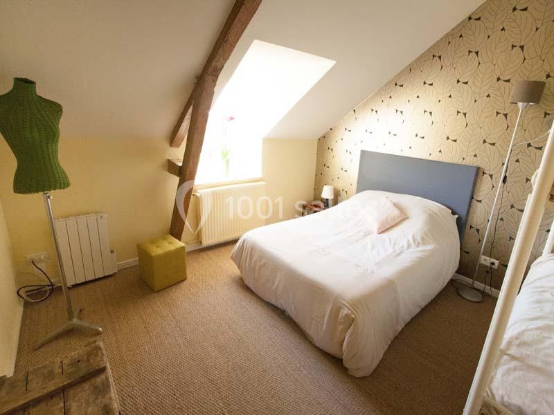 Location salle Plélan-le-Grand (Ille-et-Vilaine) - Domaine Le 5b #27 Chambre mansardée avec lit double, mur tapissé, mannequin de couture et lumière naturelle provenant d'une fenêtre.