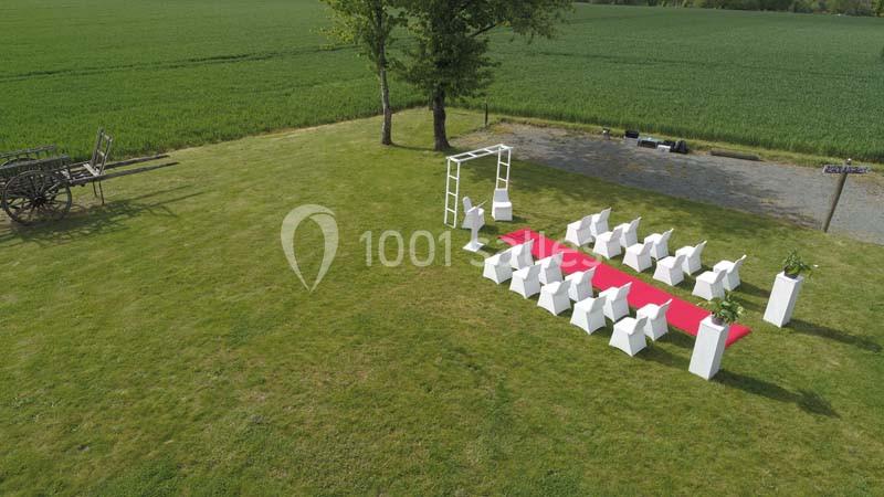 Location salle Plélan-le-Grand (Ille-et-Vilaine) - Domaine Le 5b #18 Disposition d'une cérémonie en plein air avec chaises blanches, arche décorative et tapis rouge sur une pelouse près d'un…