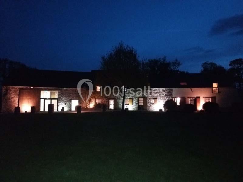 Location salle Plélan-le-Grand (Ille-et-Vilaine) - Domaine Le 5b #22 Bâtiment en pierre éclairé par des lumières extérieures, entouré d'arbres et d'une pelouse, sous un ciel nocturne.