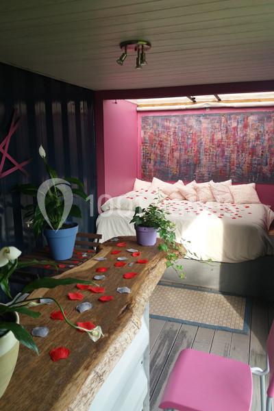 Location salle Plélan-le-Grand (Ille-et-Vilaine) - Domaine Le 5b #23 Intérieur d'une chambre colorée avec un lit décoré de pétales rouges, des plantes et une table en bois brut.