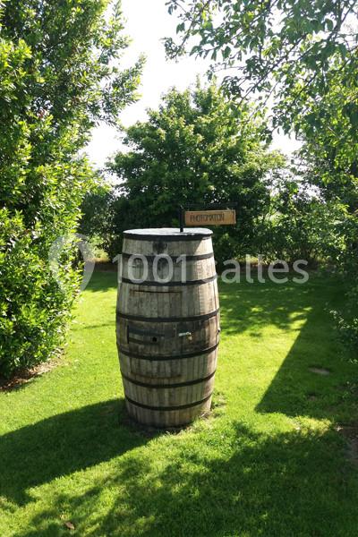 Location salle Plélan-le-Grand (Ille-et-Vilaine) - Domaine Le 5b #19 Tonneau en bois placé sur une pelouse verdoyante, entouré d'arbres, avec une pancarte indiquant ’Photomaton’.