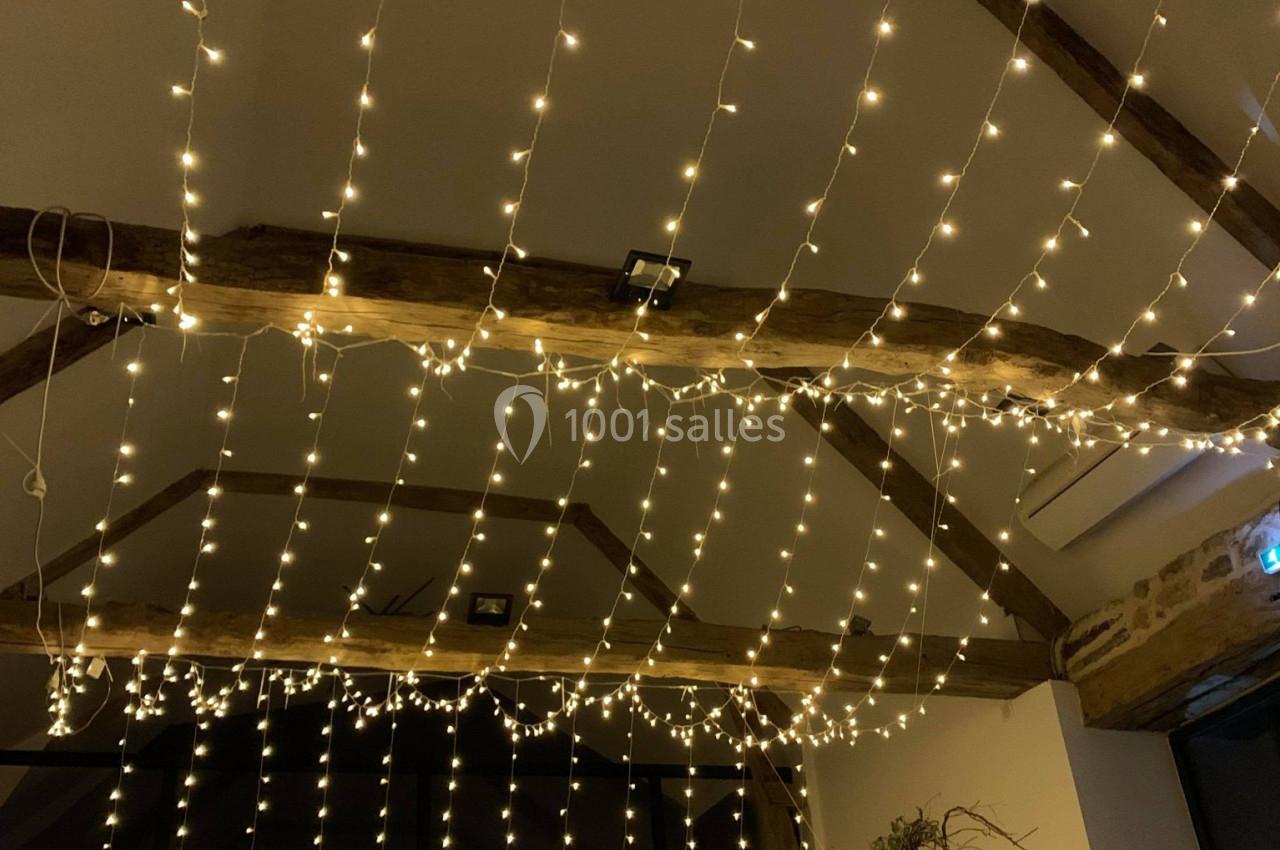 Location salle Plélan-le-Grand (Ille-et-Vilaine) - Domaine Le 5b #29 Guirlandes lumineuses suspendues au plafond d'une pièce avec poutres apparentes et décoration végétale.