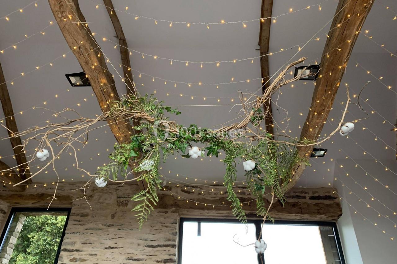 Location salle Plélan-le-Grand (Ille-et-Vilaine) - Domaine Le 5b #30 Guirlandes lumineuses suspendues à des poutres en bois avec des branches décoratives et feuillages verts.