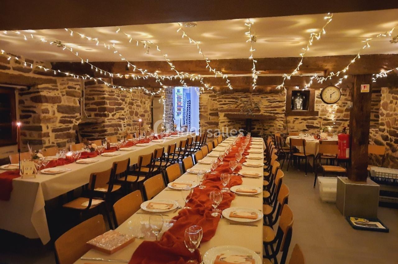 Location salle Plélan-le-Grand (Ille-et-Vilaine) - Domaine Le 5b #36 Salle décorée avec des guirlandes lumineuses, tables alignées et dressées pour un repas dans un cadre en pierre.