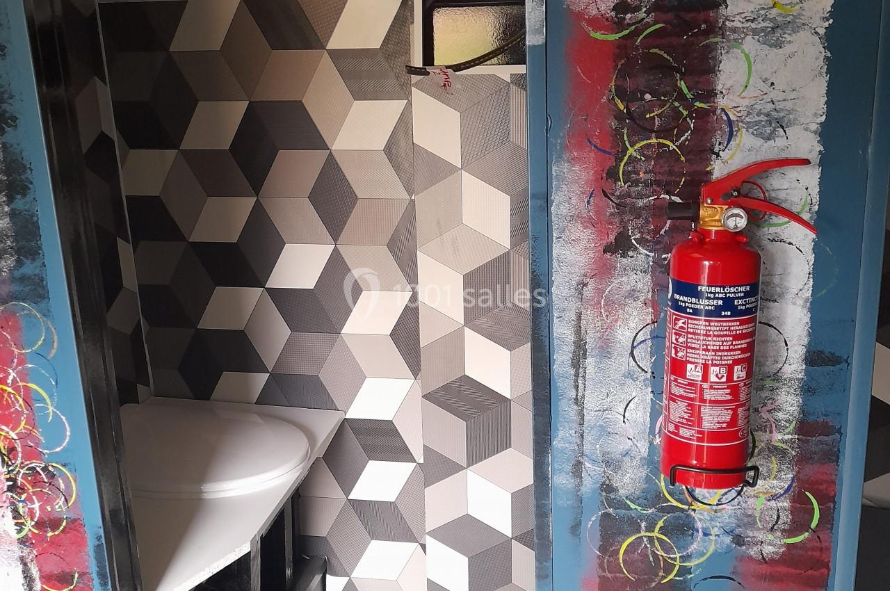 Location salle Plélan-le-Grand (Ille-et-Vilaine) - Domaine Le 5b #40 Intérieur d'un espace avec un mur en carreaux géométriques, un extincteur rouge fixé et des décorations colorées.