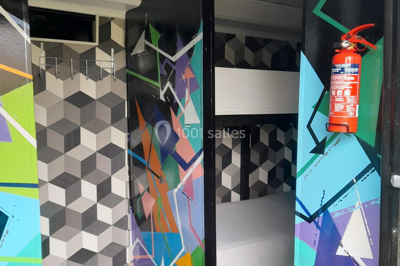 Location salle Plélan-le-Grand (Ille-et-Vilaine) - Domaine Le 5b #42 Porte colorée ouverte sur une petite chambre avec lits superposés et murs au motif géométrique.