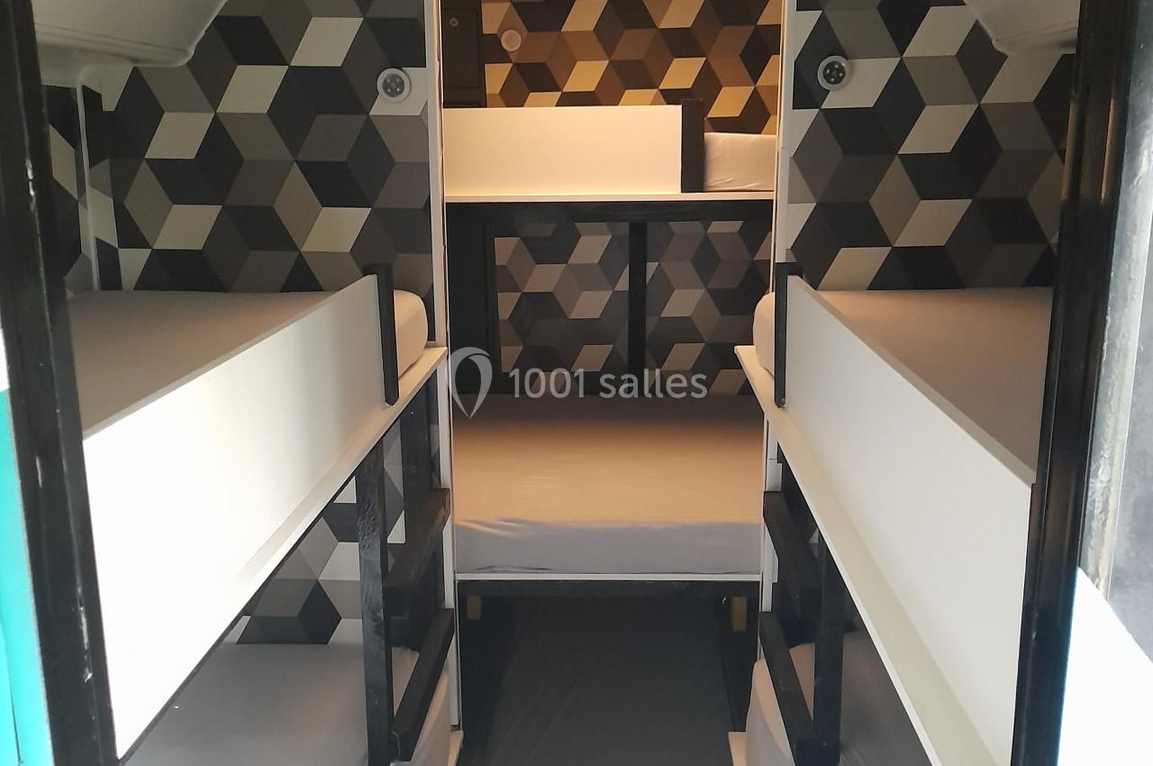 Location salle Plélan-le-Grand (Ille-et-Vilaine) - Domaine Le 5b #43 Intérieur d'un véhicule aménagé avec quatre lits superposés et un espace de rangement au fond, décor géométrique.
