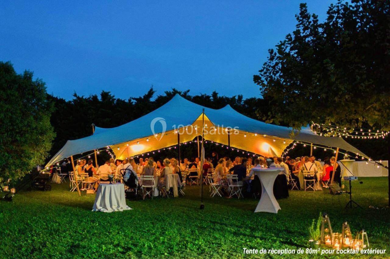 Location salle Plélan-le-Grand (Ille-et-Vilaine) - Domaine Le 5b #21 Tente éclairée abritant des invités assis à des tables lors d'une réception en soirée dans un jardin.