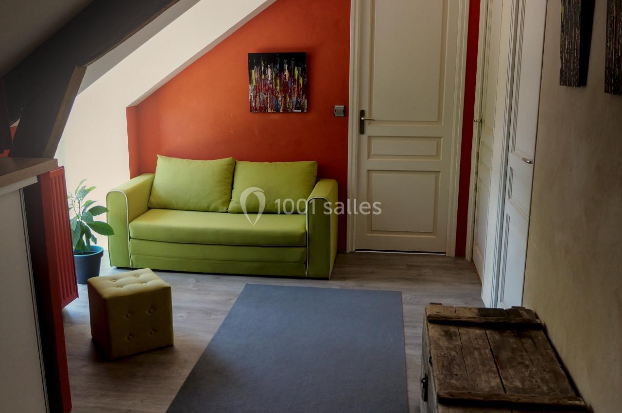 Location salle Plélan-le-Grand (Ille-et-Vilaine) - Domaine Le 5b #45 Couloir mansardé avec un mur orange, un canapé vert, des coffres en bois et une lumière naturelle provenant d'une fenêtre.