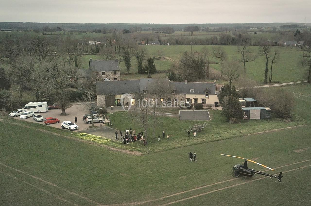 Location salle Plélan-le-Grand (Ille-et-Vilaine) - Domaine Le 5b #51 Vue aérienne d'une propriété rurale avec plusieurs bâtiments, des voitures garées et un hélicoptère posé sur un champ.