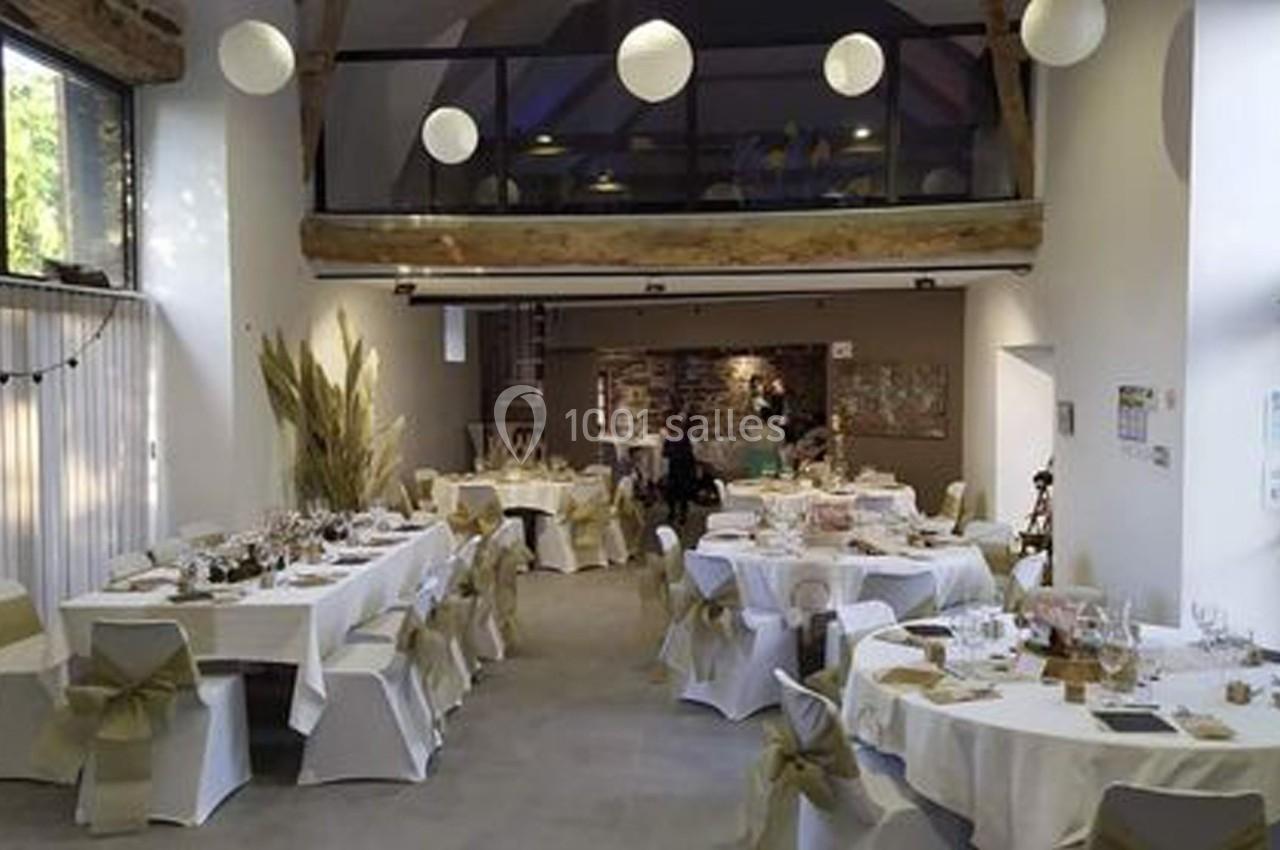 Location salle Plélan-le-Grand (Ille-et-Vilaine) - Domaine Le 5b #44 Salle de réception lumineuse avec tables décorées de nappes blanches et chaises ornées de rubans beiges.