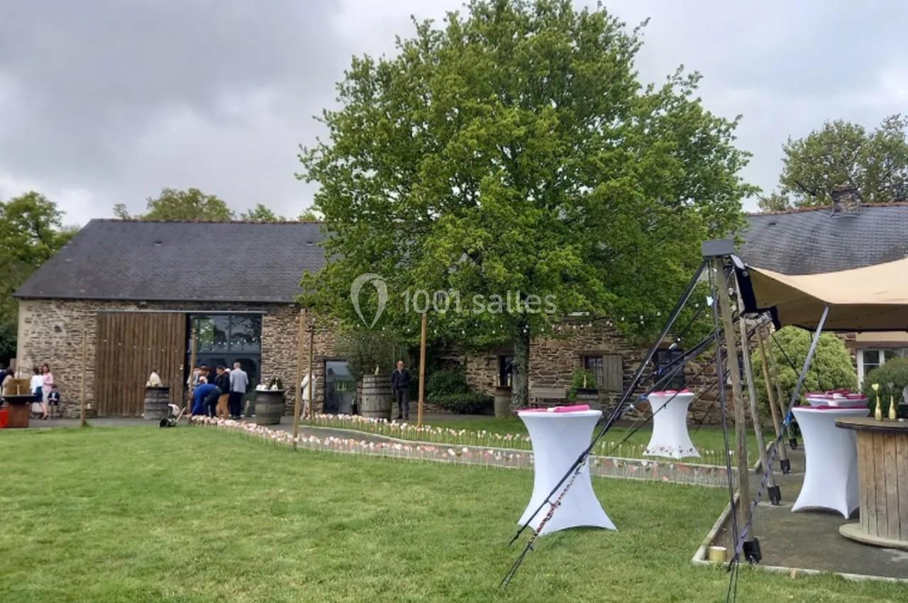 Location salle Plélan-le-Grand (Ille-et-Vilaine) - Domaine Le 5b #49 Extérieur d'une bâtisse en pierre avec pelouse, tables hautes blanches et décorations pour un événement en plein air.