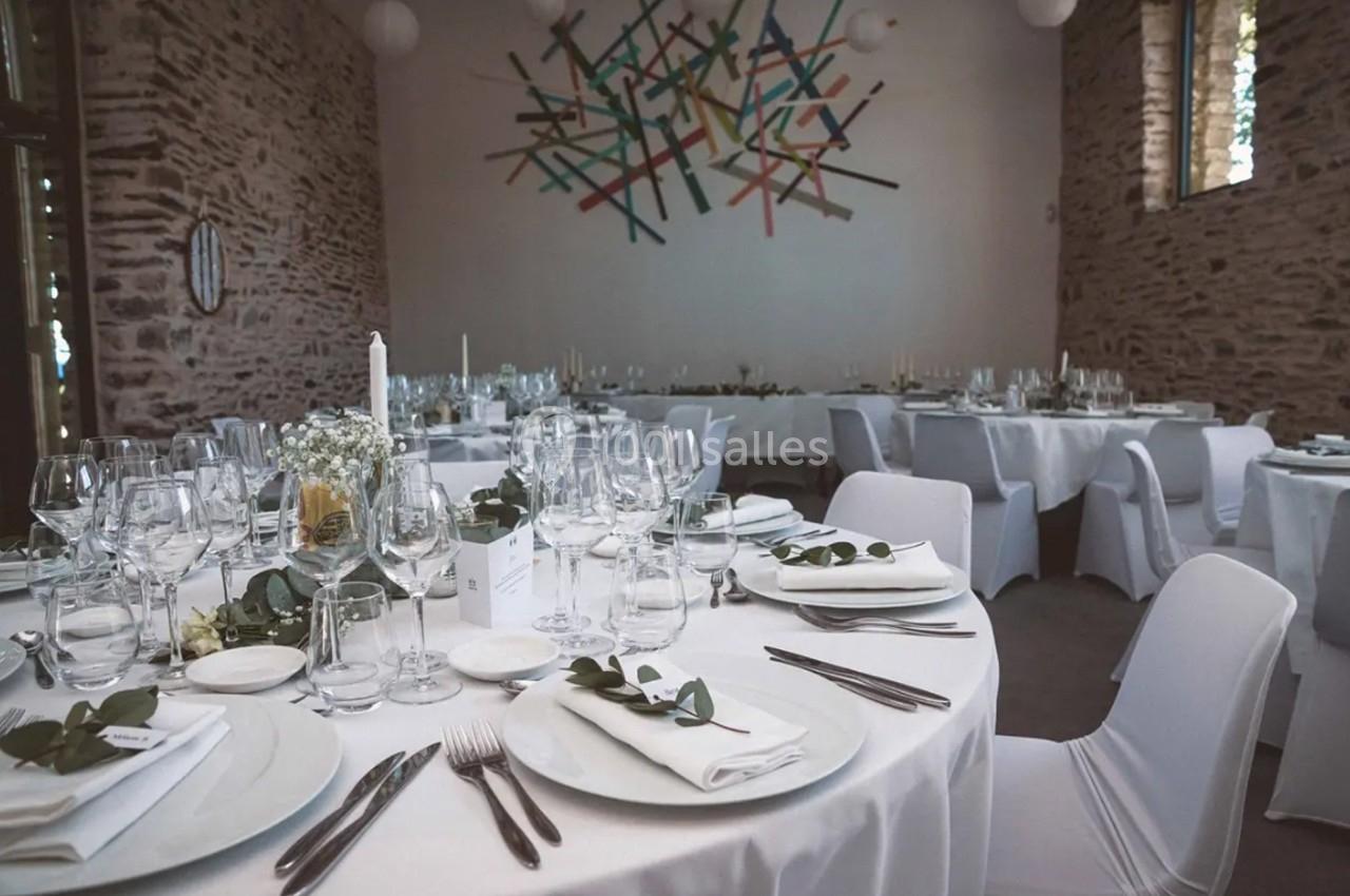 Location salle Plélan-le-Grand (Ille-et-Vilaine) - Domaine Le 5b #53 Salle de réception décorée avec des tables rondes dressées, nappes blanches et centre de table floral.