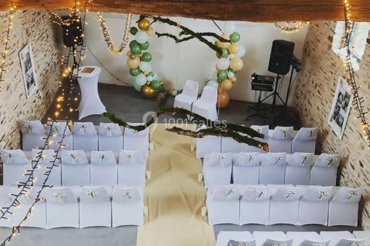 Location salle Plélan-le-Grand (Ille-et-Vilaine) - Domaine Le 5b #8 Salle décorée pour une cérémonie avec chaises blanches, arche ornée de ballons et guirlandes lumineuses suspendues.