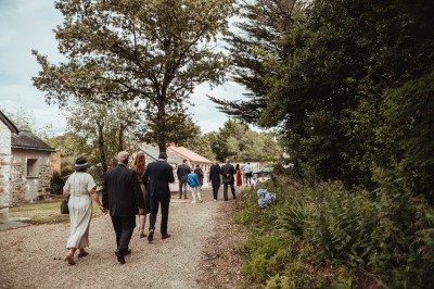 Robe de mariée en dentelle suspendue devant une fenêtre lumineuse avec vue sur un jardin verdoyant.