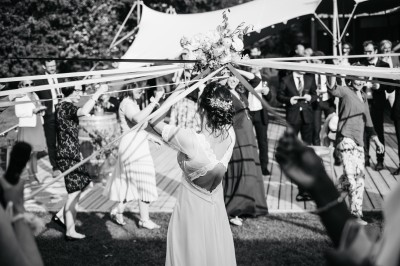 Robe de mariée en dentelle suspendue devant une fenêtre lumineuse avec vue sur un jardin verdoyant.