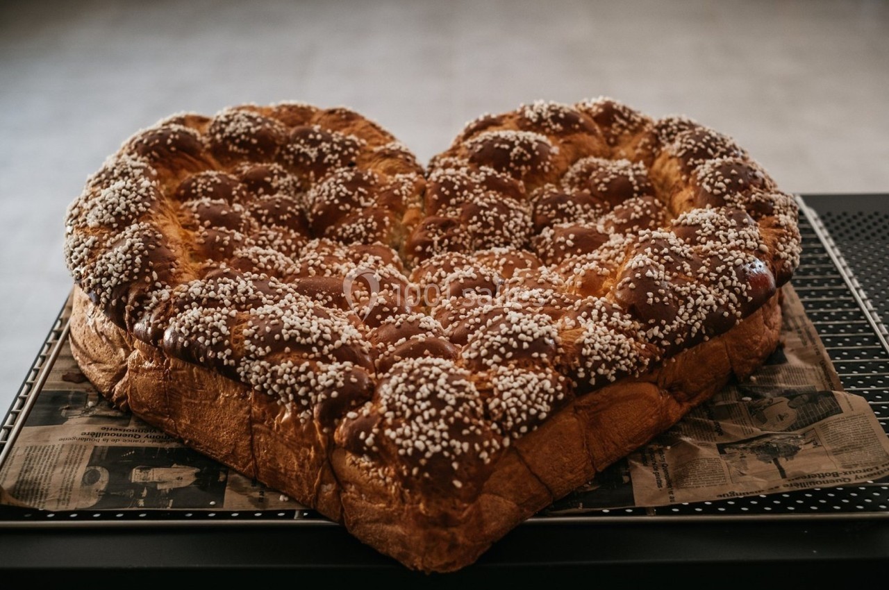 Brioche en forme de cœur, dorée et parsemée de sucre perlé, posée sur un plateau.
