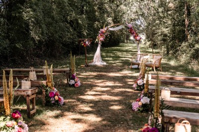 Robe de mariée en dentelle suspendue devant une fenêtre lumineuse avec vue sur un jardin verdoyant.