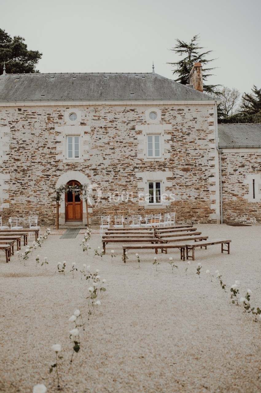 Façade en pierre d'un bâtiment ancien avec des bancs et des chaises disposés pour une cérémonie en extérieur.