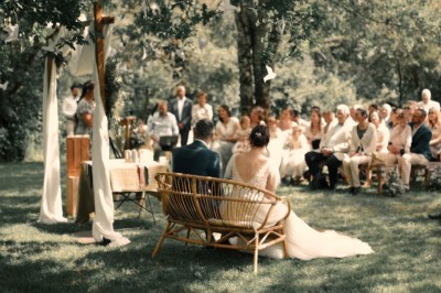 Robe de mariée en dentelle suspendue devant une fenêtre lumineuse avec vue sur un jardin verdoyant.
