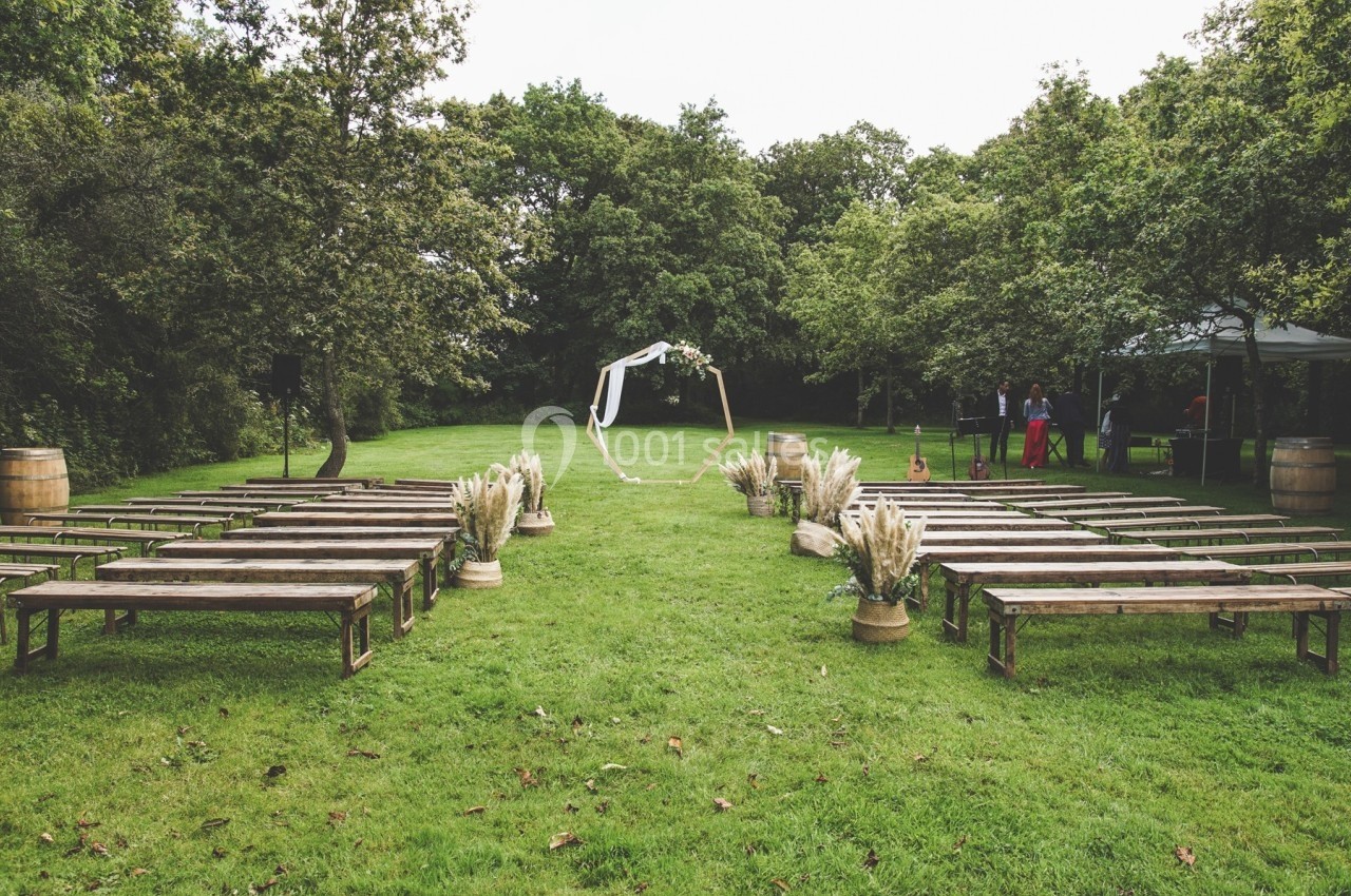 Chaises et bancs en bois disposés en extérieur pour une cérémonie, avec une arche décorée et un cadre verdoyant.