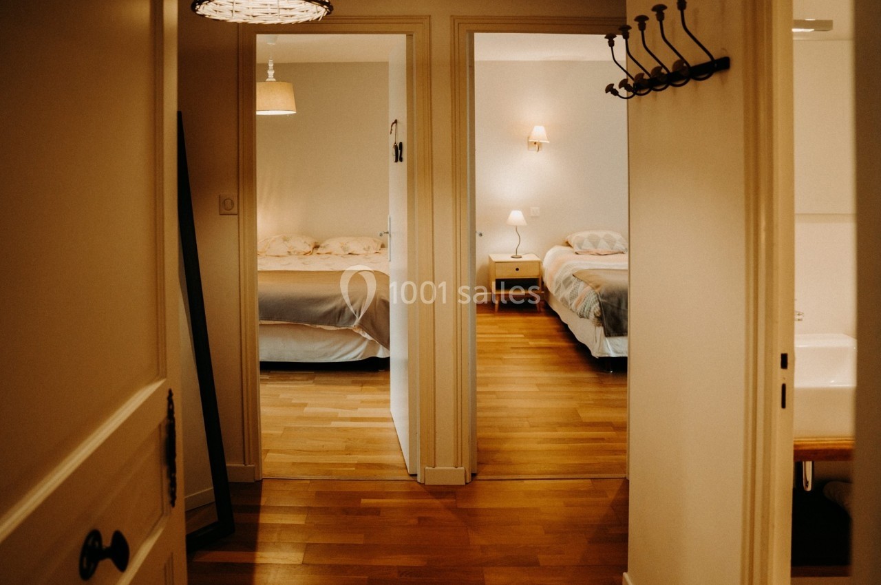 Vue d'un couloir menant à deux chambres avec lits doubles, éclairées par des lampes de chevet.