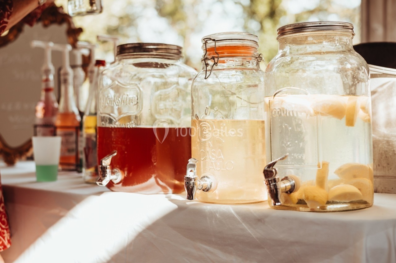 Trois distributeurs en verre contenant des boissons, dont une avec des tranches de citron, posés sur une table en extérieur.
