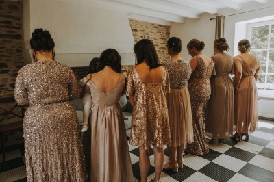 Robe de mariée en dentelle suspendue devant une fenêtre lumineuse avec vue sur un jardin verdoyant.