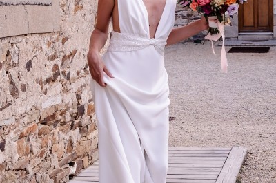 Robe de mariée en dentelle suspendue devant une fenêtre lumineuse avec vue sur un jardin verdoyant.