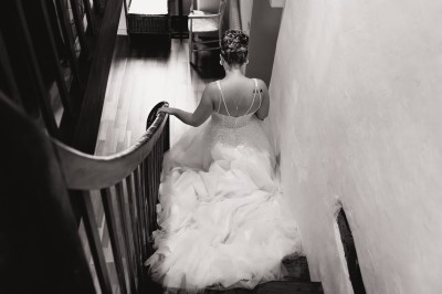 Robe de mariée en dentelle suspendue devant une fenêtre lumineuse avec vue sur un jardin verdoyant.