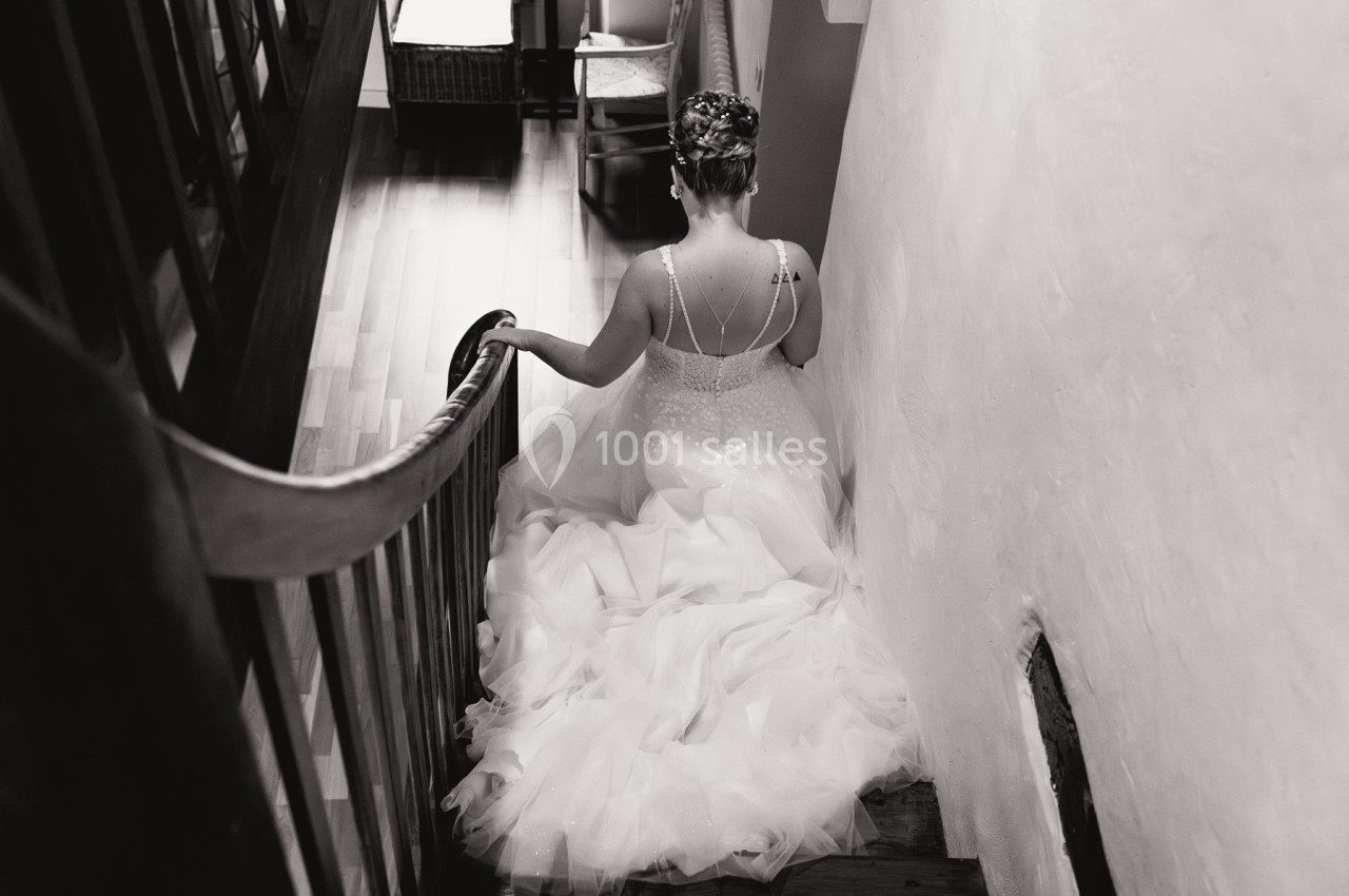 Une femme en robe de mariée descend un escalier en bois dans un intérieur lumineux.